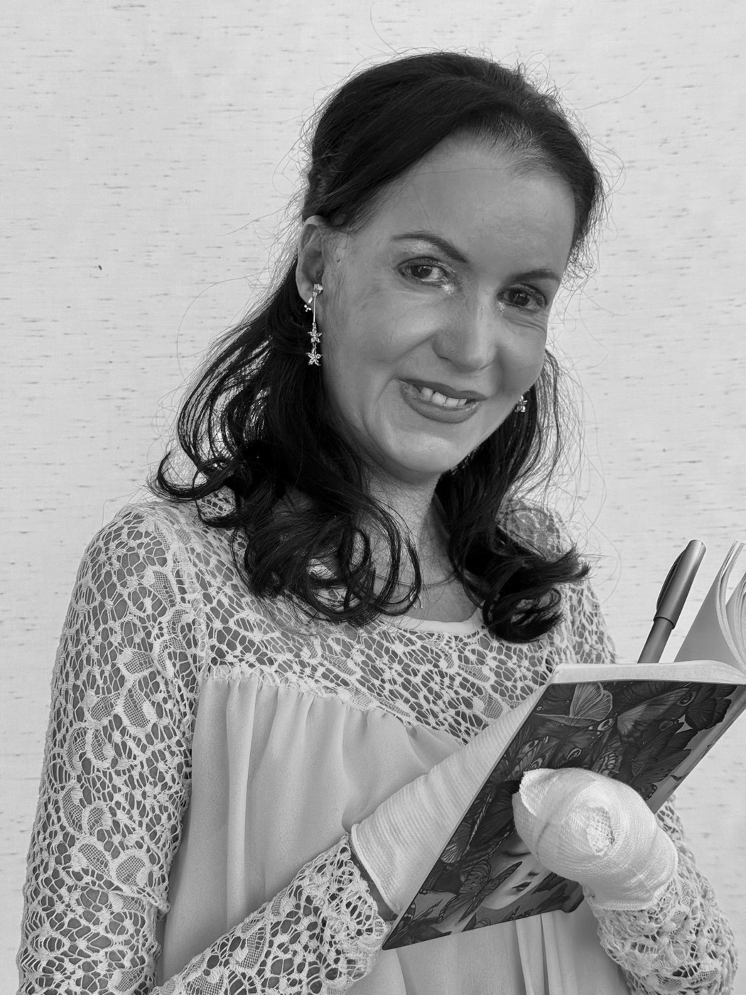 Porträt von Michelle Zimmermann: Sie hält ein aufgeschlagenes Notizbuch mit Schmetterlingen und einen Stift in der bandagierten Hand und blickt lächelnd in die Kamera.